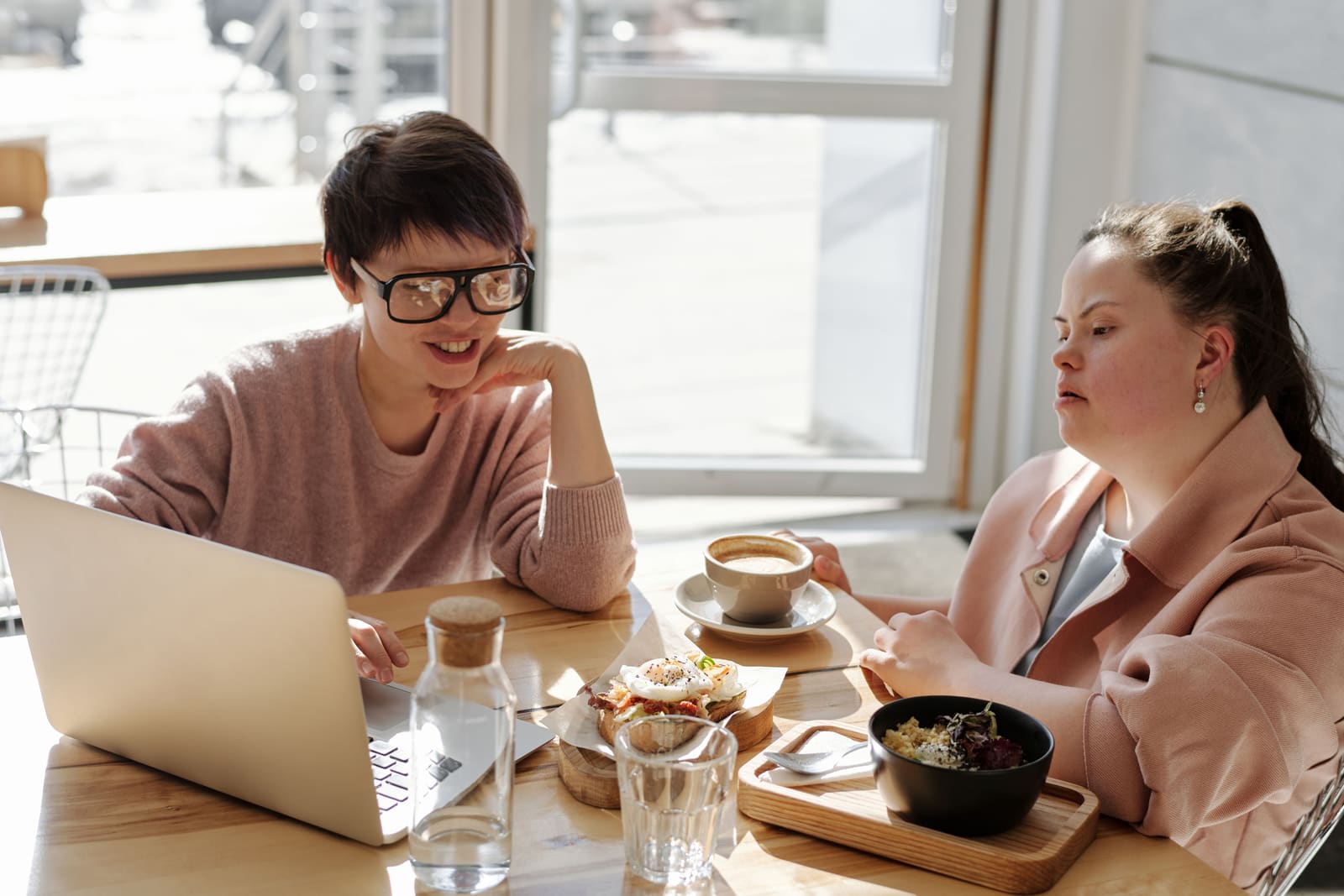 Two friends going through something on a laptop over coffee at a cafe