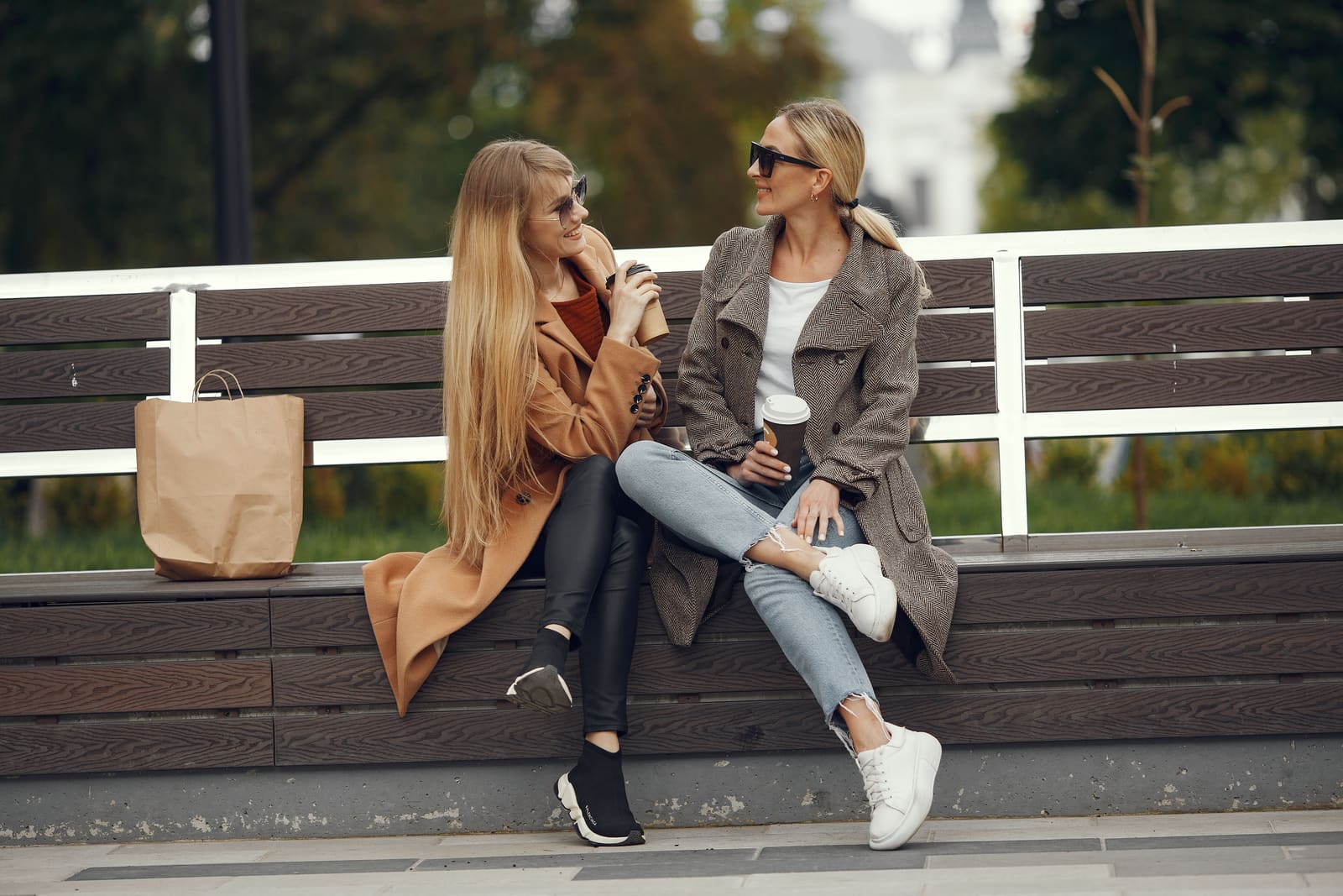 Two women talking over coffee on a bench in the sun